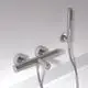 Badethermostat von Ideal Standard mit zwei Pin-Griffen und einem Handbrauseanschluss, montiert an einer weißen Wand. Chrom-Oberfläche und klar strukturiertes Design.